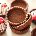 How to make Chocolate Mini Tart Shells 1 ½ cups (6.5 ounces) all-purpose flour 2/3 cup (3 ounces) powdered sugar ¼ cup (0.5 ounce) Dutch cocoa ¼ teaspoon salt ½ cup (4 ounces) cold butter, grated 1 large egg, cold and beaten 2-3 tablespoons ice water In a mixing bowl (or food processor), whisk together flour, powdered sugar, cocoa and salt. Add cold, grated butter, and mix with beaters (or food processor) until mixture looks like pebbly sand. Add egg and ice water (1 tablespoon at a time), and mix on low speed just until it begins to form clumps. Use hands to form into a ball, handling only as much as necessary, then flatten slightly. Dust work surface and top of dough with cocoa, and gently roll pastry to about 1/8 inch thickness, turning often and dusting with more cocoa as needed. Cut 3 ½ inch circles (or circles slightly larger than muffin tin openings), and using a spatula, gently transfer them to muffin tin, pressing into corners to form shells. Cover and chill 2 hours or overnight. DO NOT skip the chilling! Preheat oven to 350 degrees F. Prick bottoms of shells a few times with a fork. Place cupcake liners into pastry, and fill with rice or pie weights. Bake 15 minutes. Remove cupcake liners, and bake another 2-3 minutes. Allow to cool in pan 2-3 minutes, and then carefully remove and transfer to wire rack to cool completely. Makes 12 chocolate mini shells